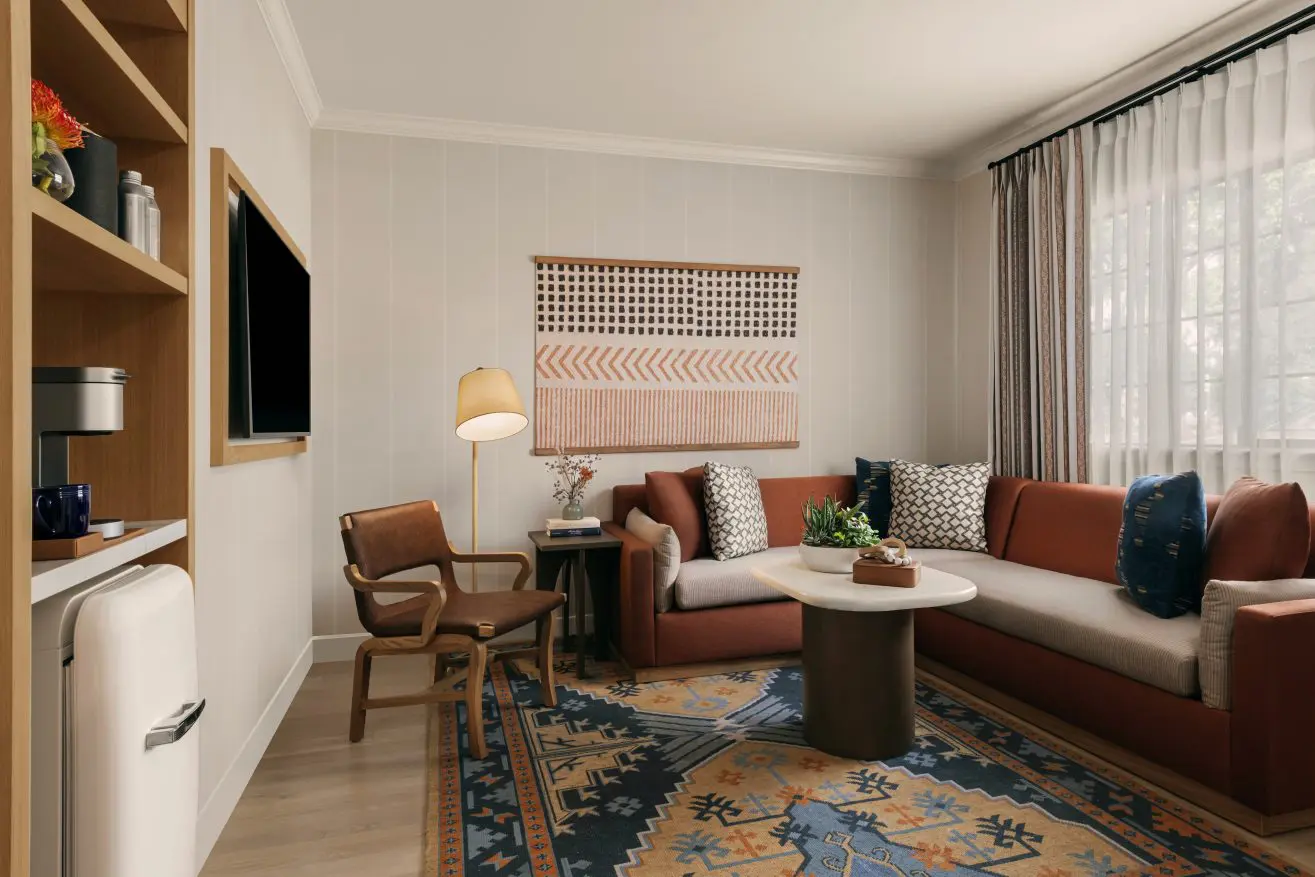 Living room with a colorful tapestry, couch, chair, table, and colorful rug.