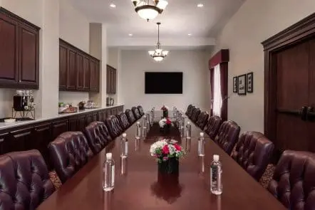 A modern meeting room with a long wooden table, comfortable chairs, large windows, and vibrant artwork on the walls.