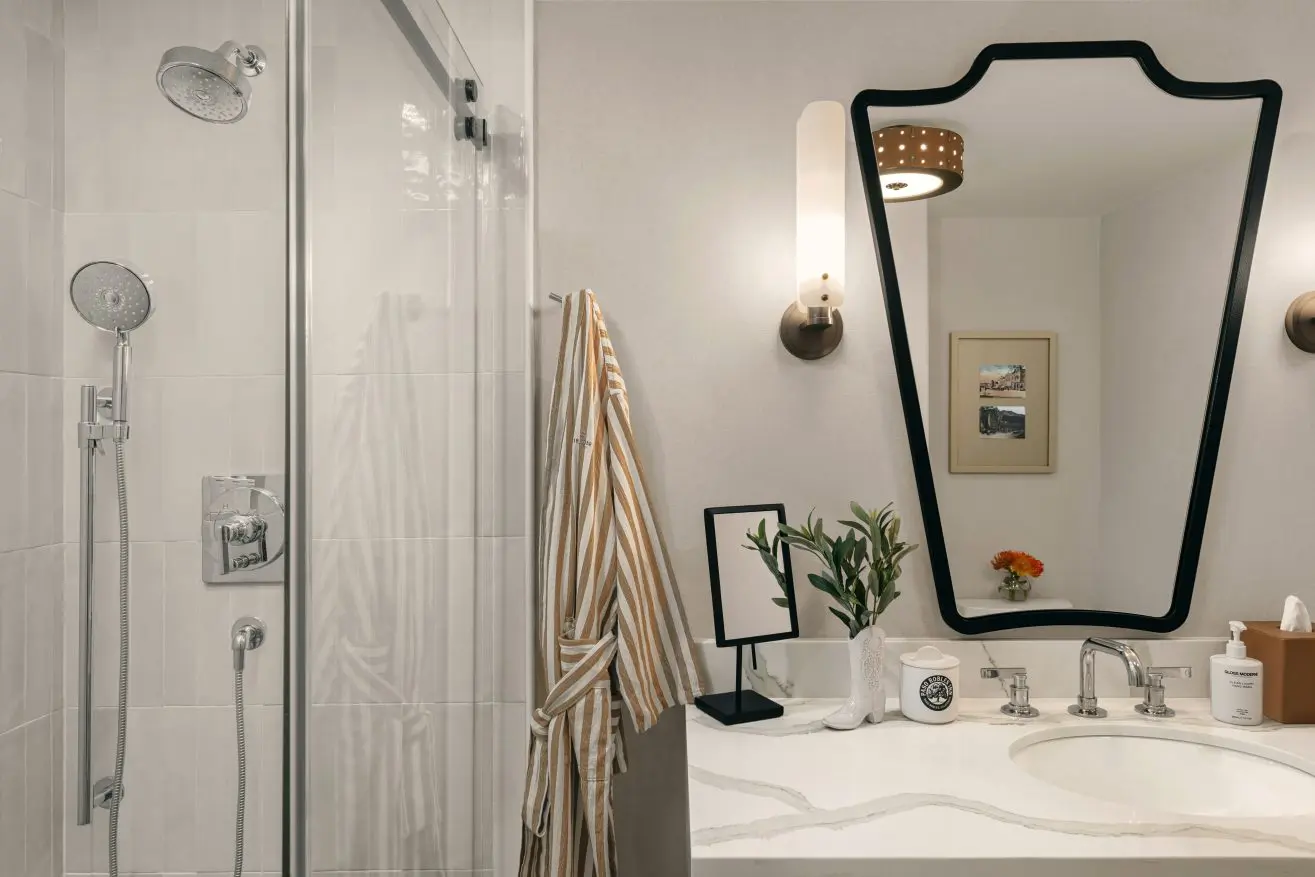 Park Room Bathroom at Paso Robles Inn with black framed vanity mirror, striped bath robe, black framed magnifying mirror, and shower.