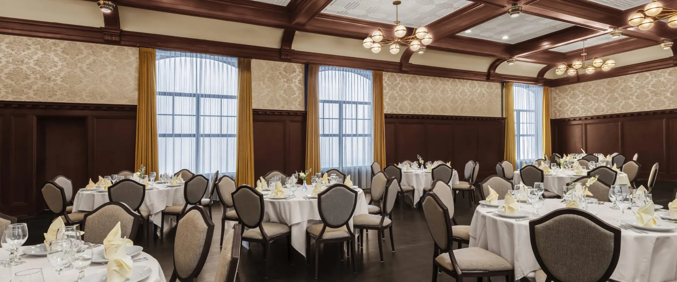 Round tables in ballroom with white linen and dark flooring.