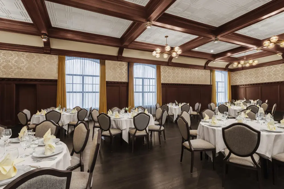 Round tables in ballroom with white linen and dark flooring.