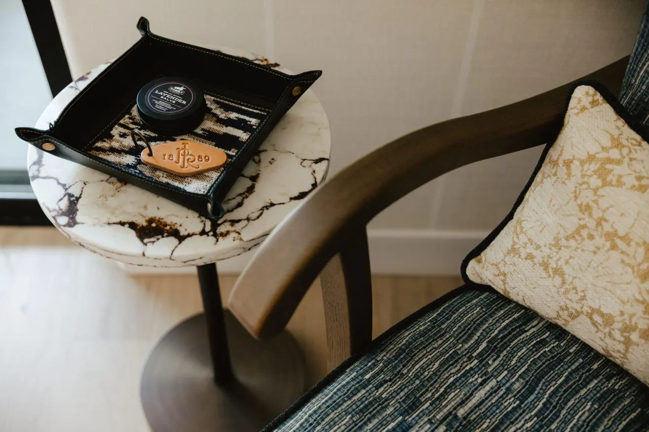 Chair and side table with cowhide basket holding lavender balm and Paso Robles Inn keychain.