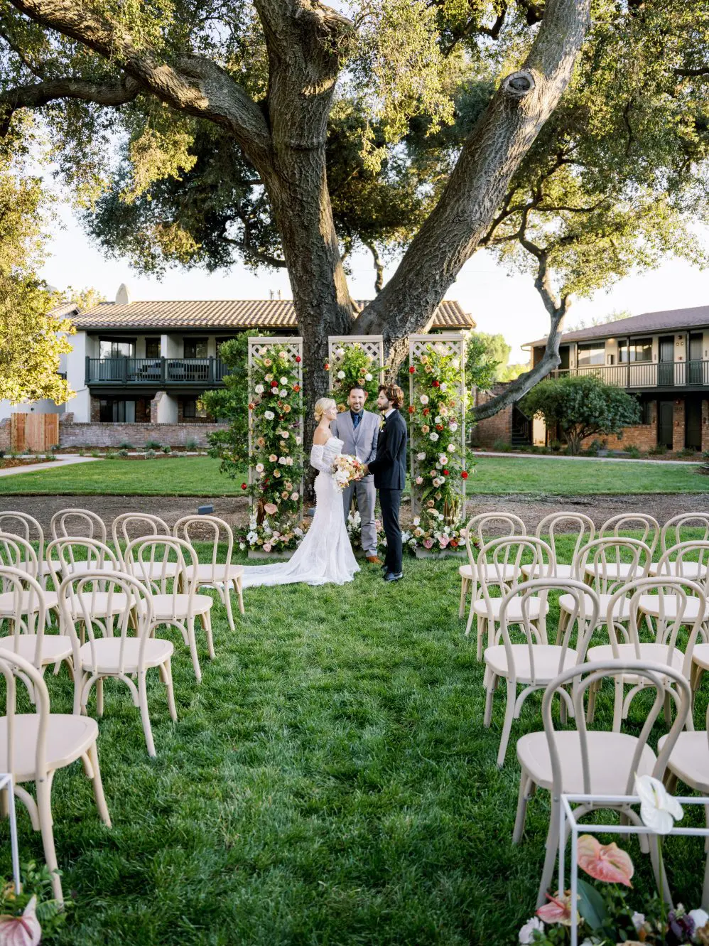 Officiant marrying a bride and groom in a garden under a sprawling oak tree.