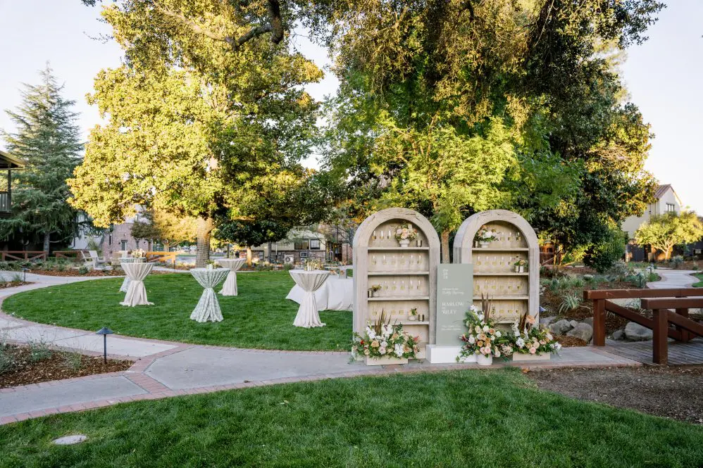 Garden filled with wedding high top tables and large wooden arches filled with glasses of champagne and florals