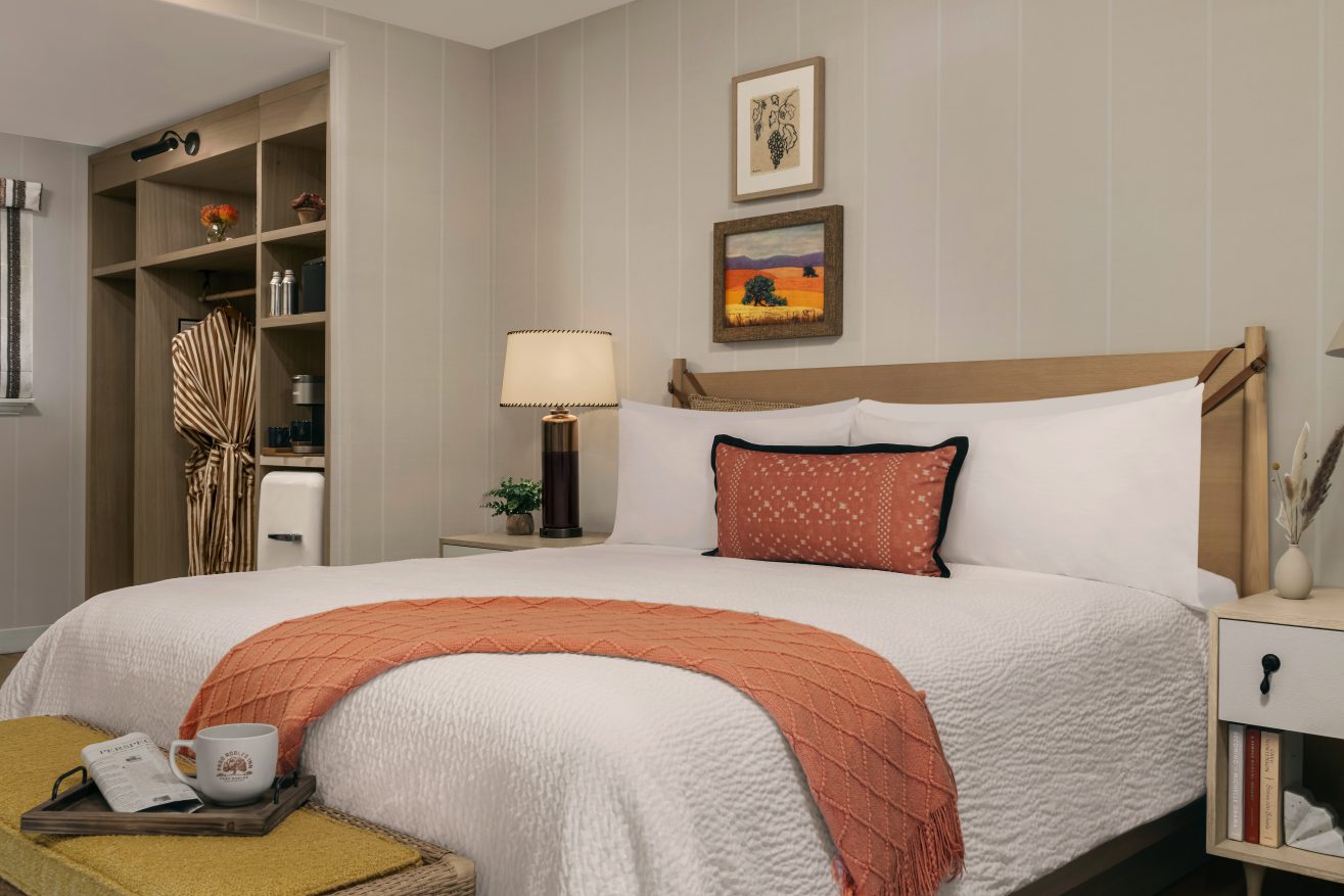 Garden Room at Paso Robles Inn with orange throw blanket on bed and coffee mug and newspaper on the bench in front of the bed.
