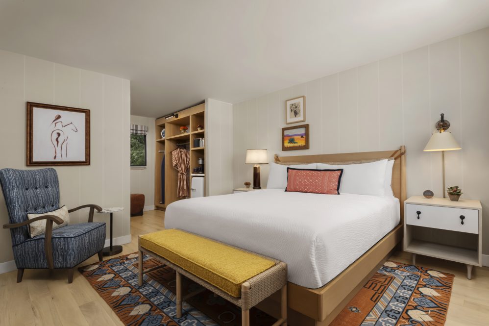 Garden King Room at Paso Robles Inn. White bedding, yellow bench, orange accent pillow, wall art on the walls.