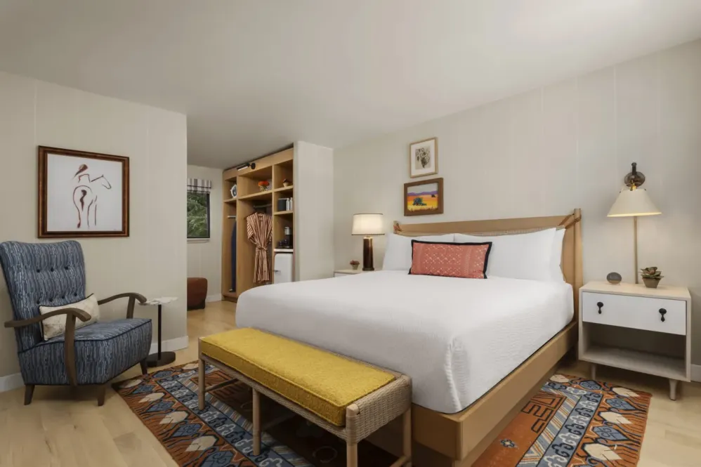 Garden King Room at Paso Robles Inn. White bedding, yellow bench, orange accent pillow, wall art on the walls.