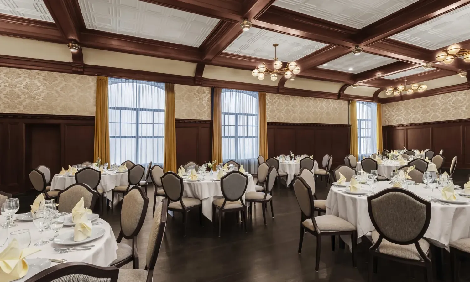 Round tables in ballroom with white linen and dark flooring.