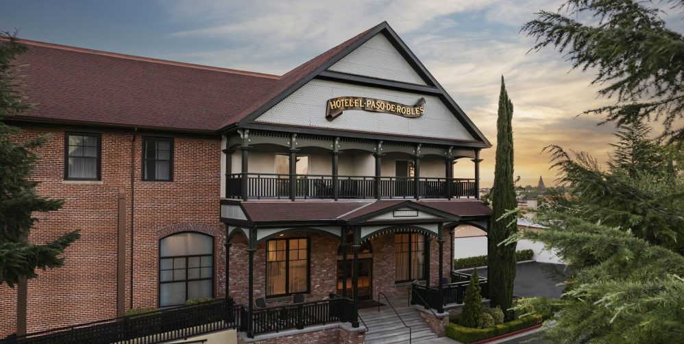 A historic brick building with a large front porch and sign reading Hotel Paso Robles, surrounded by trees at sunset.