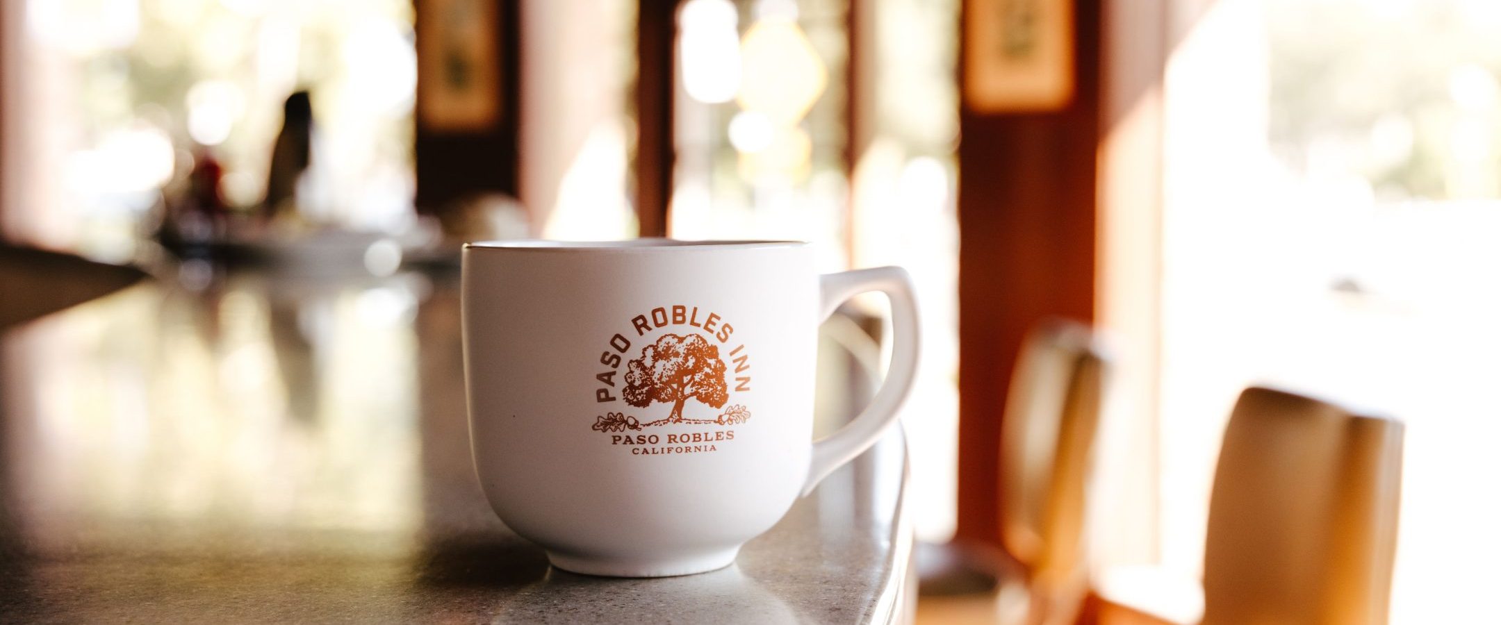 Paso Robles Inn branded coffee mug sitting on counter of coffee shop.