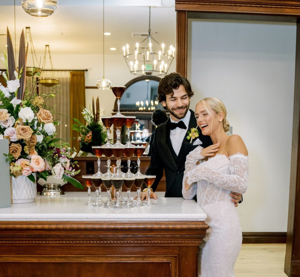 A bride and groom laughing next to an espresso martini tower.