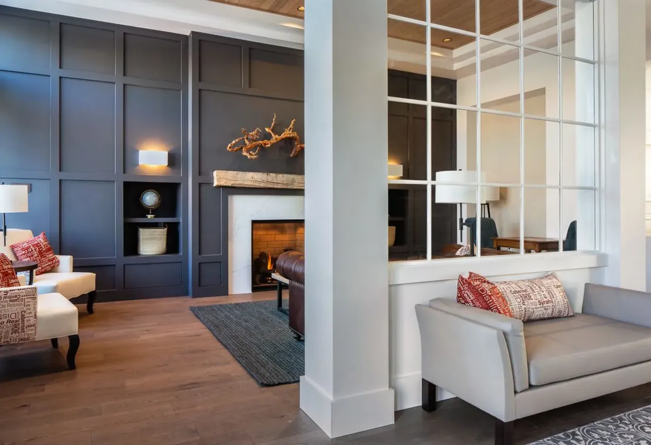Modern living room with dark paneled accent wall, fireplace, and comfortable seating. Neutral tones, patterned pillows, wood flooring, and a decorative branch above the mantel create a cozy, stylish atmosphere.