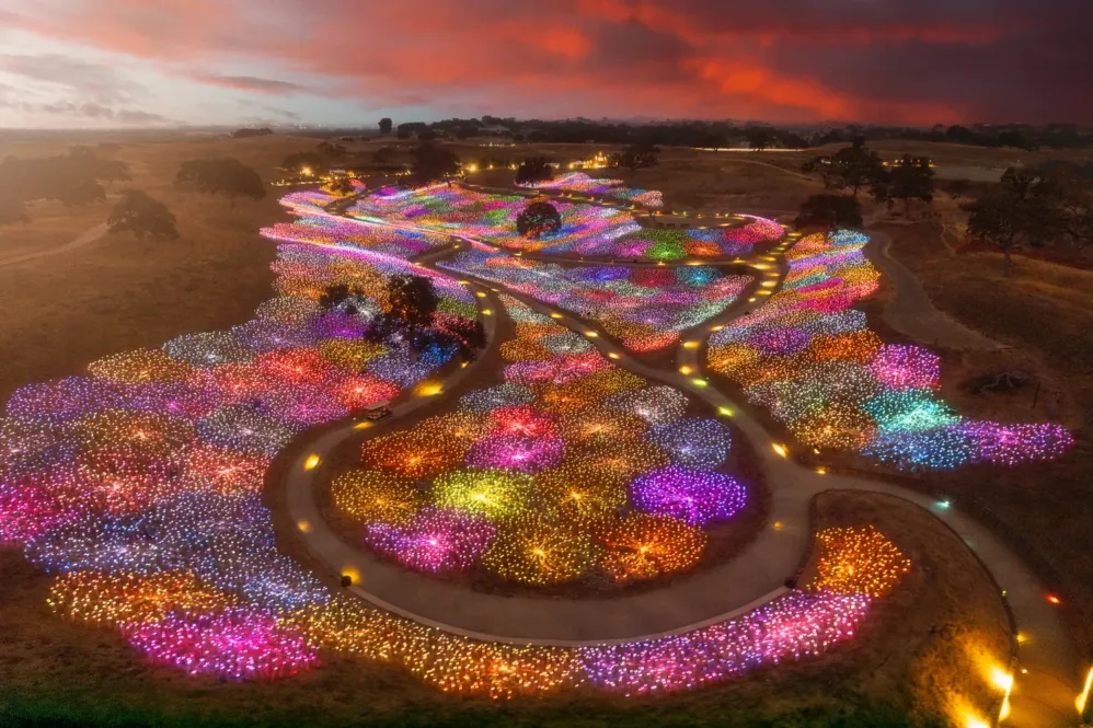 Aerial view of rolling hills covered in clusters of colorful, glowing lights at sunset, with winding pathways illuminated through the vibrant landscape installation—an enchanting scene inspired by The Sensorio Stay Package - Paso Robles Inn.