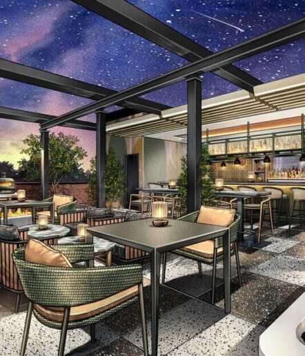 A stylish rooftop restaurant with cozy seating, modern tables, and warm lighting under a glass roof. The night sky above is filled with stars, creating a relaxing and inviting atmosphere.