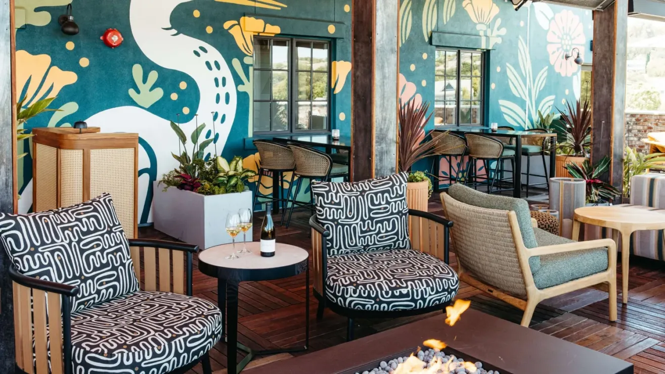Outdoor patio at Salina Rooftop with patterned black-and-white chairs, a fire pit, tables, and drinks. The vibrant mural, greenery, and sunlight create a relaxed atmosphere perfect for unwinding above the city.